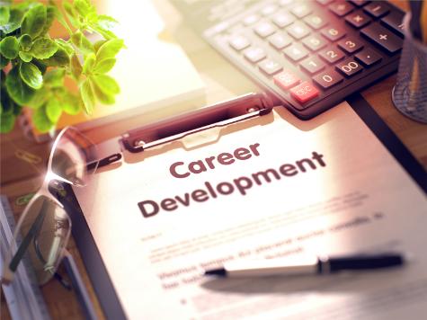 Clipboard on desk with calculator, plant, and glasses, and sun filtering in. Paper in clipboard has headline 'Career Development' with pen laying on paper.