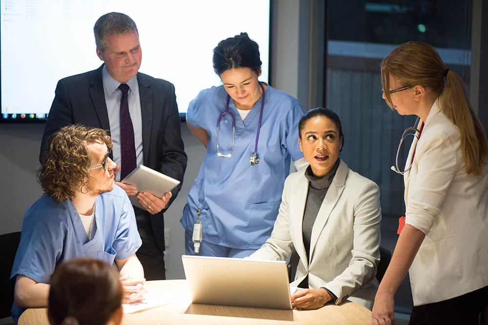 a man and woman in a suit meeting with medical professionals around a laptop.