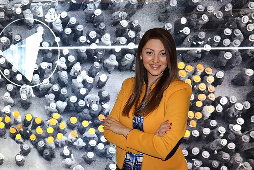 Esther Elkouss standing in front of a large screen displaying a street scene from above