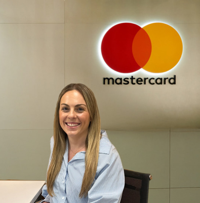 GSB alum Jessica Lilly sitting at desk with MasterCard logo in the background